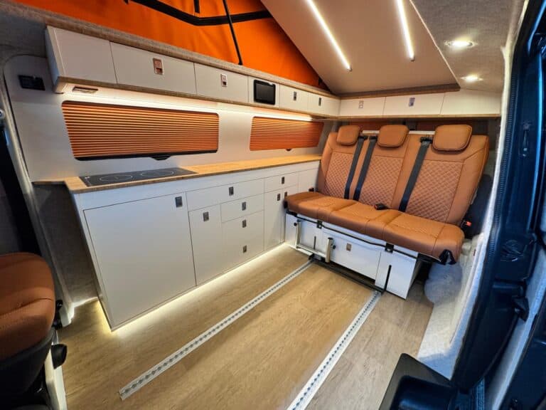 Camper van interior with kitchenette, grey cupboards, orange trim and tan quilted bench seat