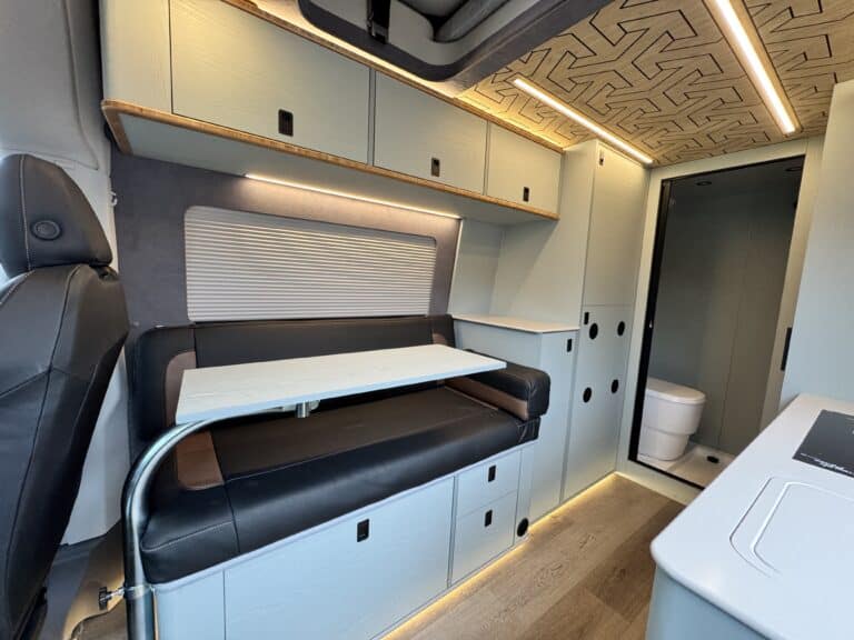 Compact van interior featuring a kitchen area, seating, storage cabinets, and a bathroom space.